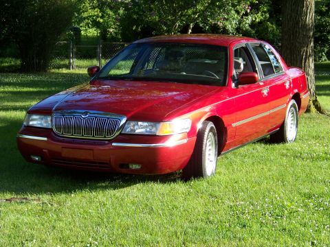 1999 Mercury Grand Marquis - A red 1999 Mercury Grand Marquis is parked on a sunny day in a grassy area with trees.