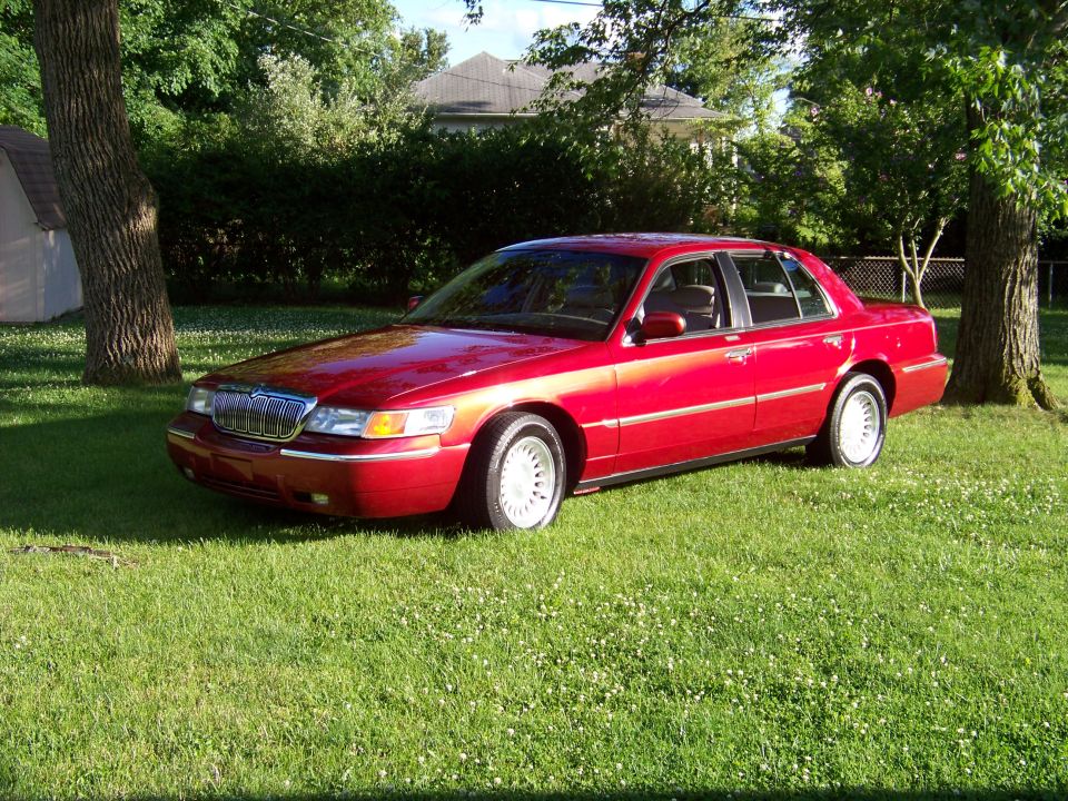 Red sedan parked on grass, front 3/4 view. Grille and headlights visible