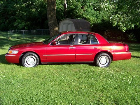 1999 Mercury Grand Marquis - Red 1999 Mercury Grand Marquis sedan sits on a grassy lawn with trees and a shed in the background.