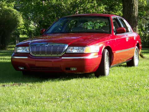 1999 Mercury Grand Marquis - A red 1999 Mercury Grand Marquis is parked on a sunny day in a grassy area with trees.