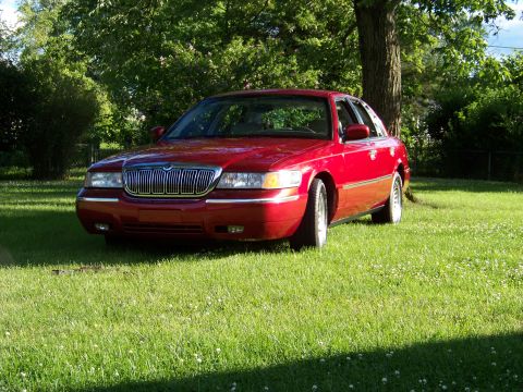 1999 Mercury Grand Marquis - A red 1999 Mercury Grand Marquis is parked on a lawn in front of a tree.