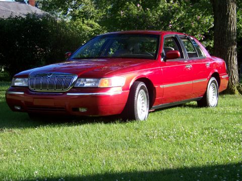 1999 Mercury Grand Marquis - Red 1999 Mercury Grand Marquis sedan parked on a grassy lawn next to a tree.
