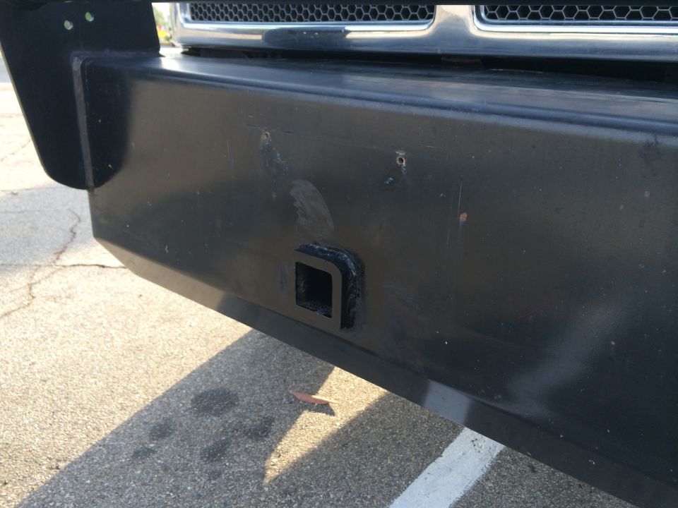 Close-up of a black heavy-duty front bumper with a square tow hitch receiver opening