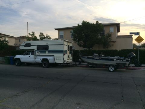1997 Dodge 3500 - A white pickup truck tows a boat trailer on a street with houses in the background.