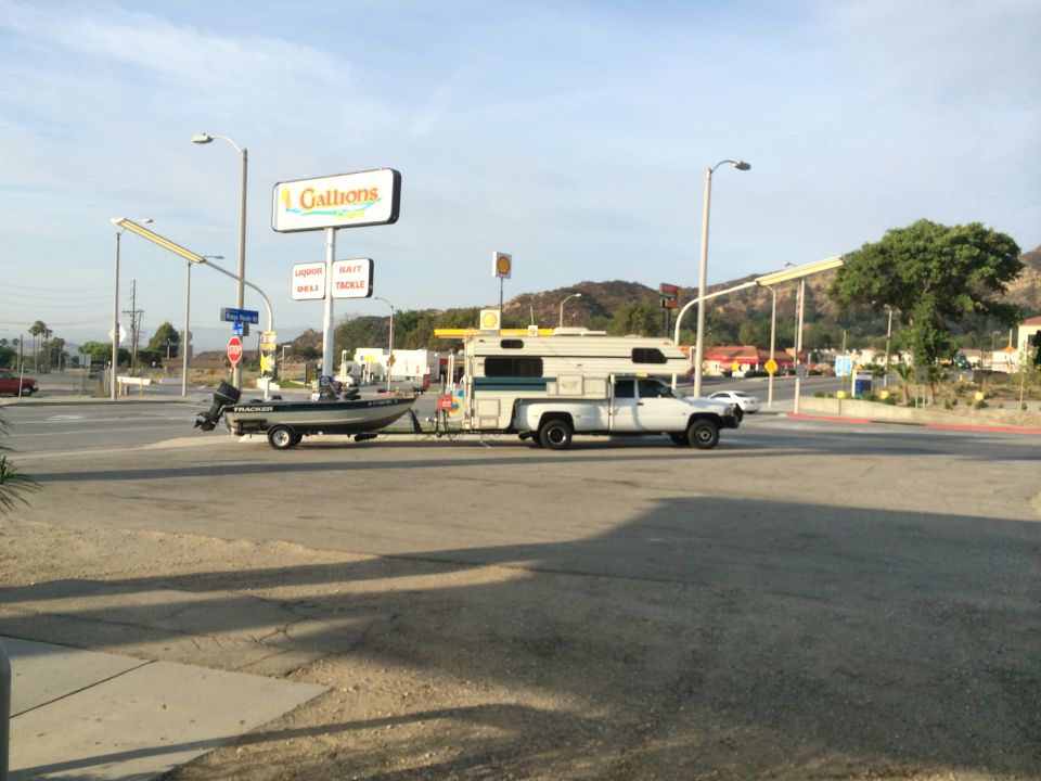 1997 Dodge 3500 pickup truck with camper shell towing a boat trailer at a gas station