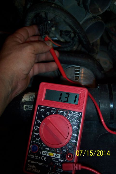 1990 Ford Bronco - A hand uses a multimeter to test voltage in an engine bay, with the meter displaying 1.31 volts.