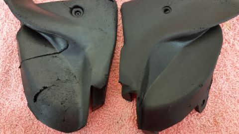1973 Chevrolet Camaro - A pair of black plastic automotive parts, one showing significant cracking and damage, are displayed on a pink textured background.