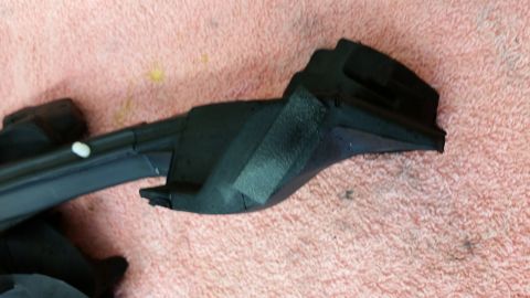 1973 Chevrolet Camaro - Close-up of a black plastic automotive part, possibly a trim piece, on a pink textured surface.