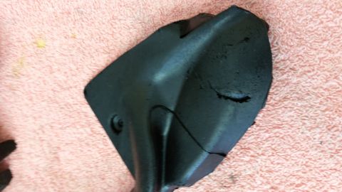 1973 Chevrolet Camaro - A damaged black plastic automotive part is shown against a pink textured background.