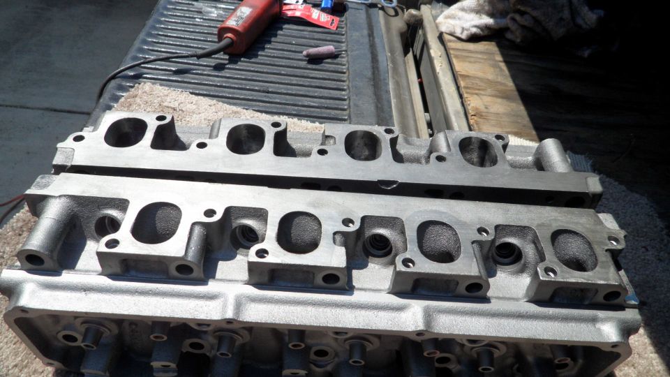 Two engine cylinder heads on a truck bed, with a rotary tool in the background