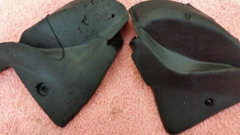 1973 Chevrolet Camaro - Two damaged black plastic automotive parts are displayed against a pink textured background.