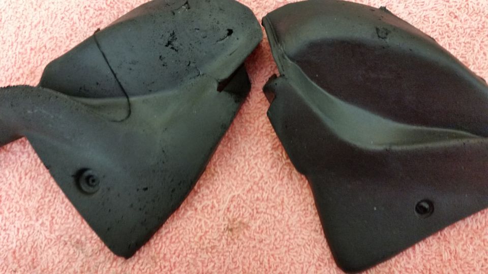 Two black plastic car parts with textured surfaces and visible damage, resting on a pink textured surface