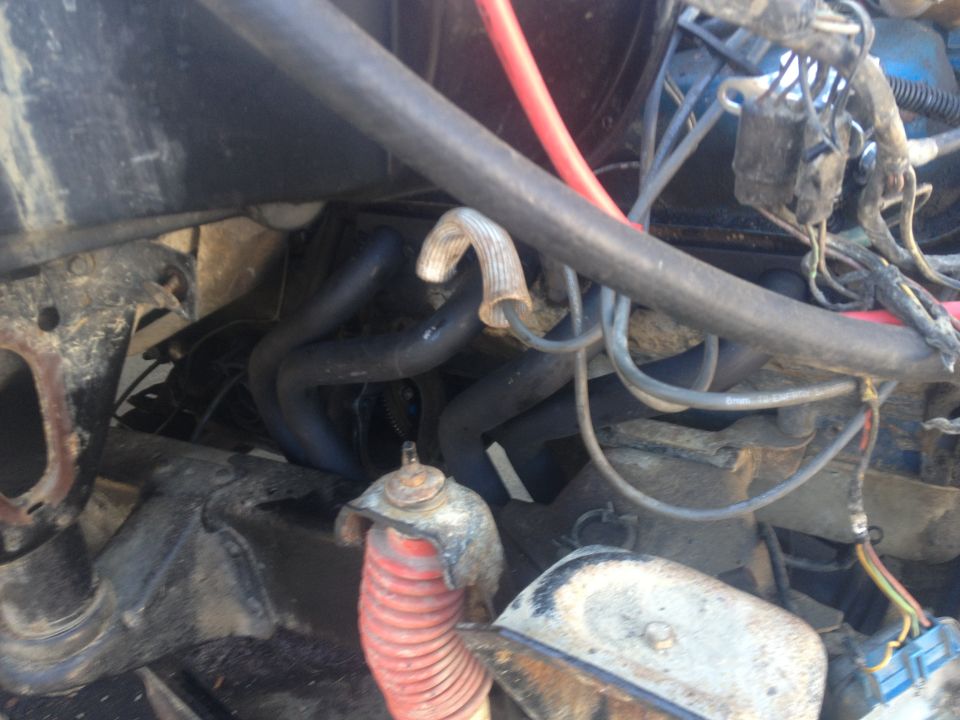 Close-up of engine bay showing exhaust manifold, hoses, and wiring