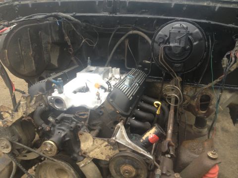 Engine bay with V8 engine, intake manifold, and exhaust headers. Some wiring and hoses visible