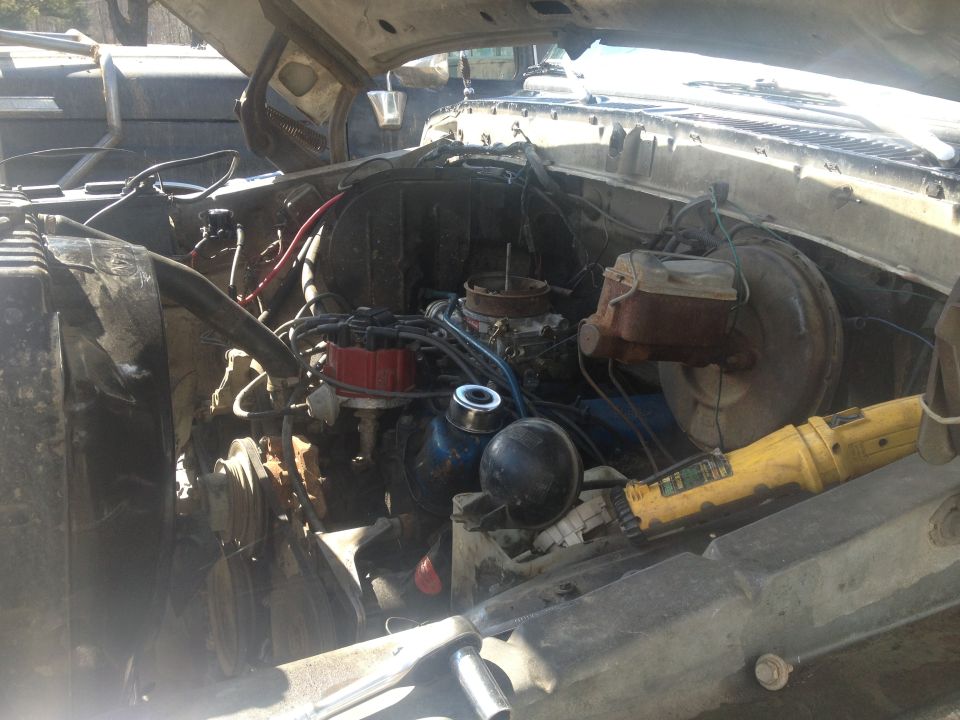 Engine bay with V8 engine, carburetor, and brake booster. Yellow power tool on fender