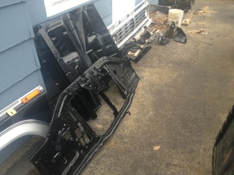Black metal car frame assembly and a chrome grille leaning against a blue wall