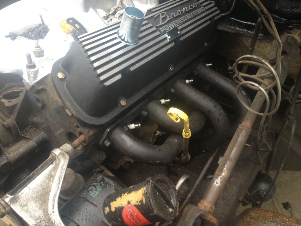 Engine valve cover with 'Bronco POWERED BY FORD' text. Exhaust manifolds and spark plugs visible