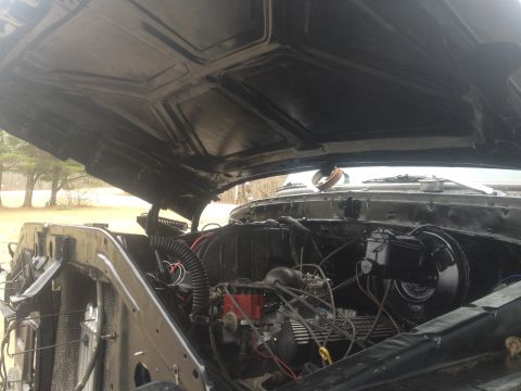 Black engine bay with hood open, showing engine components and radiator. Watermark reads SUPERMOTORS.NET