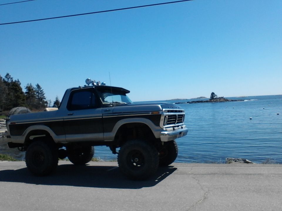 Lifted Ford Bronco parked by the water, with off-road lights on the roof visor
