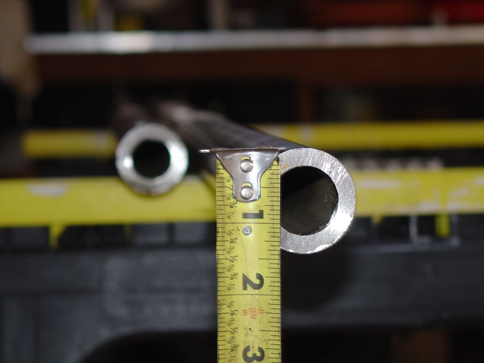 Yellow tape measure held against the end of a thick-walled steel tube, measuring its diameter on a workbench