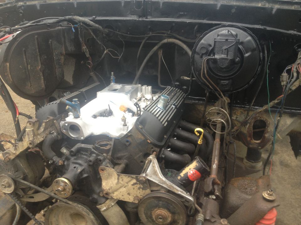 Engine bay with V8 engine, intake manifold, and exhaust manifolds visible. Some wiring and hoses are present