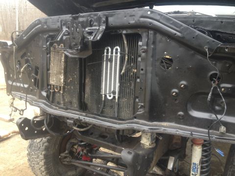 Front end of a vehicle with hood open, showing radiator and engine components. Tires and suspension visible be