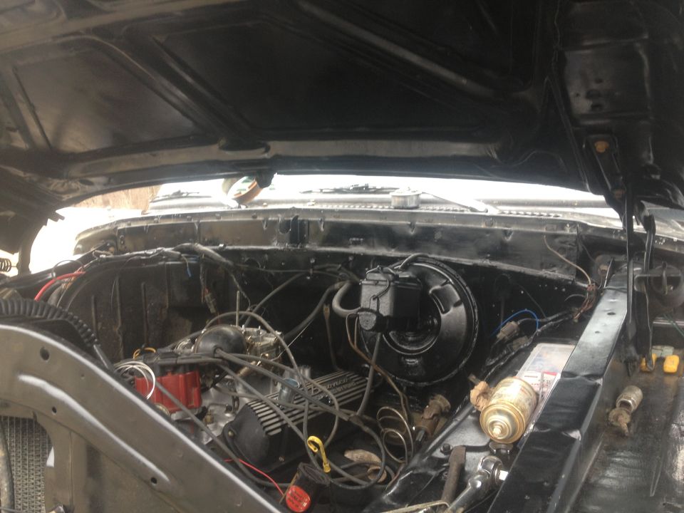 Black engine bay with exposed engine components, wiring, and brake master cylinder