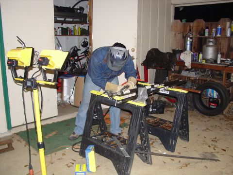 1979 Ford Bronco - A person welds a metal frame in a cluttered garage setting.