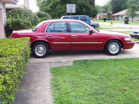 1999 Mercury Grand Marquis - A red sedan is parked on a concrete driveway next to a manicured hedge.
