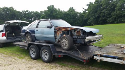 1991 Ford Crown Victoria LTD - A damaged Ford Mustang is being transported on a trailer, with a white SUV visible behind it.