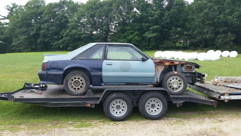 1991 Ford Crown Victoria LTD - A damaged Ford Mustang is transported on a trailer, its front end removed and body showing signs of wear.