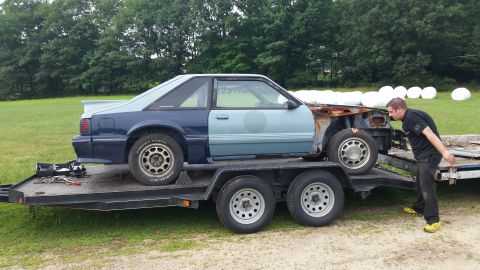 1991 Ford Crown Victoria LTD - A two-tone Ford Mustang is loaded onto a trailer, missing its front end.