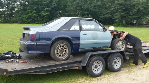 1991 Ford LTD Crown Victoria - A person works on the front of a two-tone Ford Mustang being transported on a trailer.