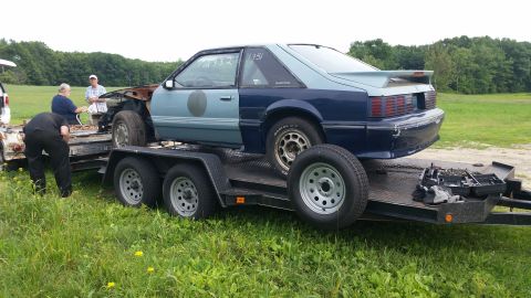 1991 Ford LTD Crown Victoria - A two-tone blue Ford Mustang is loaded onto a trailer, missing its front end and showing signs of modification.
