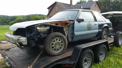 1991 Ford LTD Crown Victoria - This damaged coupe, possibly a Ford Mustang, is being transported on a trailer with its front end disassembled.