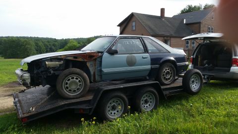 1991 Ford LTD Crown Victoria - A damaged Ford Mustang is being transported on a trailer, accompanied by an SUV.