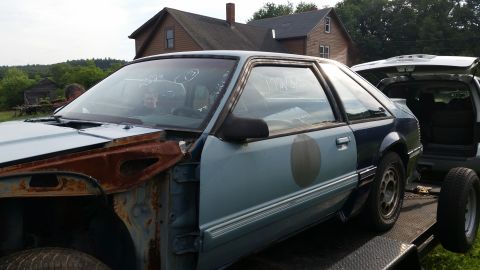 1991 Ford LTD Crown Victoria - A light blue Ford Mustang coupe, missing its front fender and showing signs of rust, is loaded onto a trailer.
