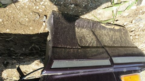 1991 Ford LTD Crown Victoria - A close-up view of a damaged dark purple rear bumper corner with a gray trim strip.