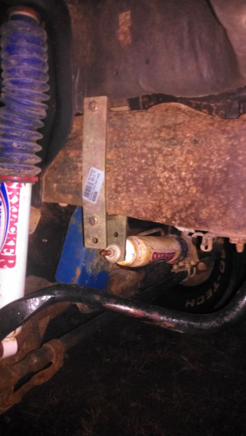 1990 Ford Bronco - Close-up view of a steering stabilizer assembly, a blue shock absorber and visible metal parts.