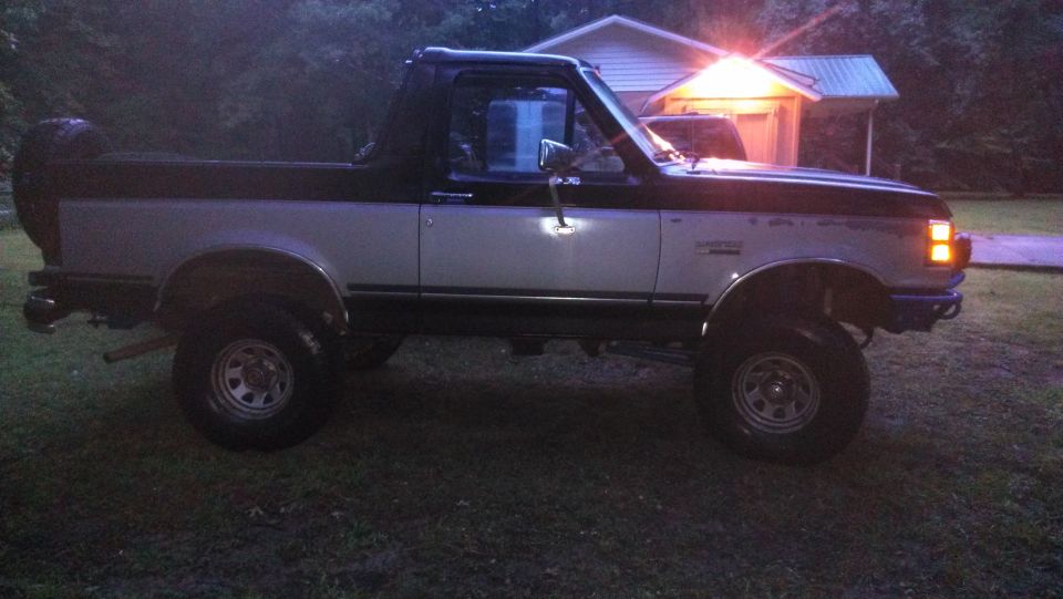 1990 Ford Bronco parked on grass, side view. Two-tone paint, spare tire on rear