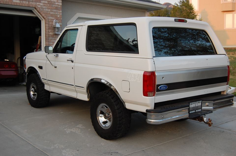 White Ford Bronco with aftermarket wheels and tires, seen from the rear quarter angle