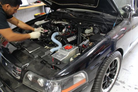 2003 Ford Crown Victoria - gloved mechanic leans into the engine bay of a black car fitted with a supercharged engine and a blue silicone hose.