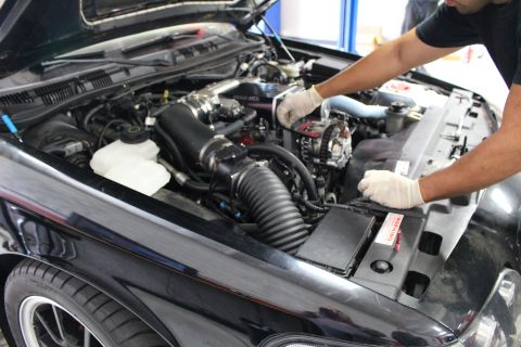 2003 Ford Crown Victoria - gloved mechanic leans over the right side of a black car engine bay with black corrugated intake tubing and a battery.