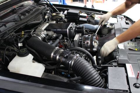 2003 Ford Crown Victoria - supercharged engine bay of a black car showing a Kenne Bell blower, alternator, intake tubing and a battery warning label.