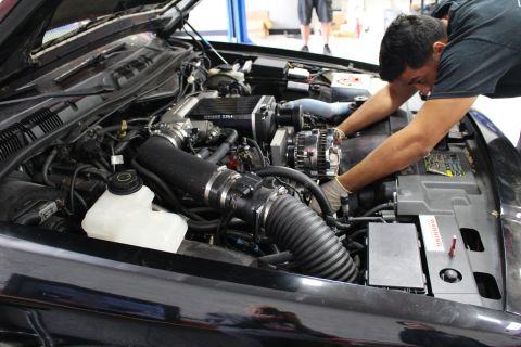 2003 Ford Crown Victoria - mechanic reaches into the engine bay of a black car fitted with a Kenne Bell supercharger and black intake tubing.