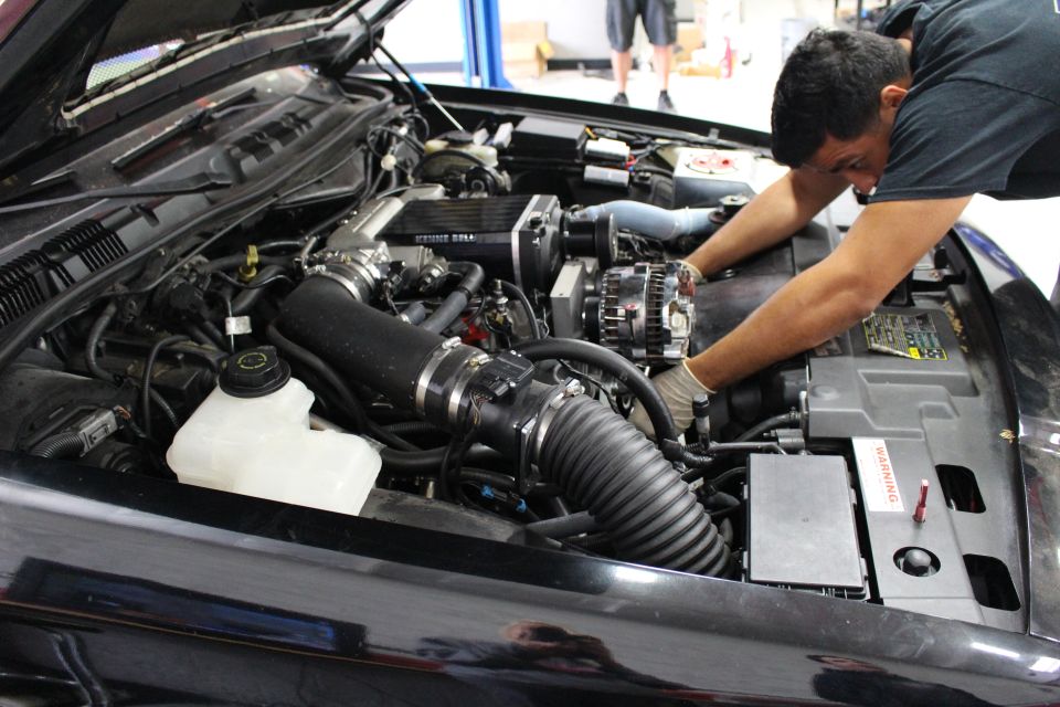 Mechanic reaching deep into the supercharged engine bay of a black car
