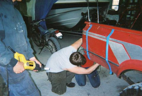 1978 Ford Bronco - Two individuals are working on the red bed of a pickup truck, which has silver trim and is secured with blue tape.