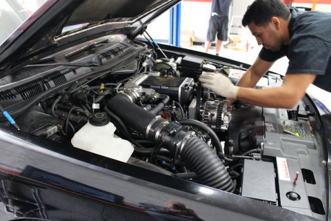 2003 Ford Crown Victoria - mechanic leans over the supercharged engine bay of a black car with a Kenne Bell blower and black intake tubing.