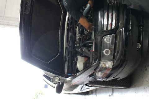 2003 Ford Crown Victoria - Front corner of a lowered black Ford sedan with a projector-style headlight and hood raised, a mechanic working alongside.