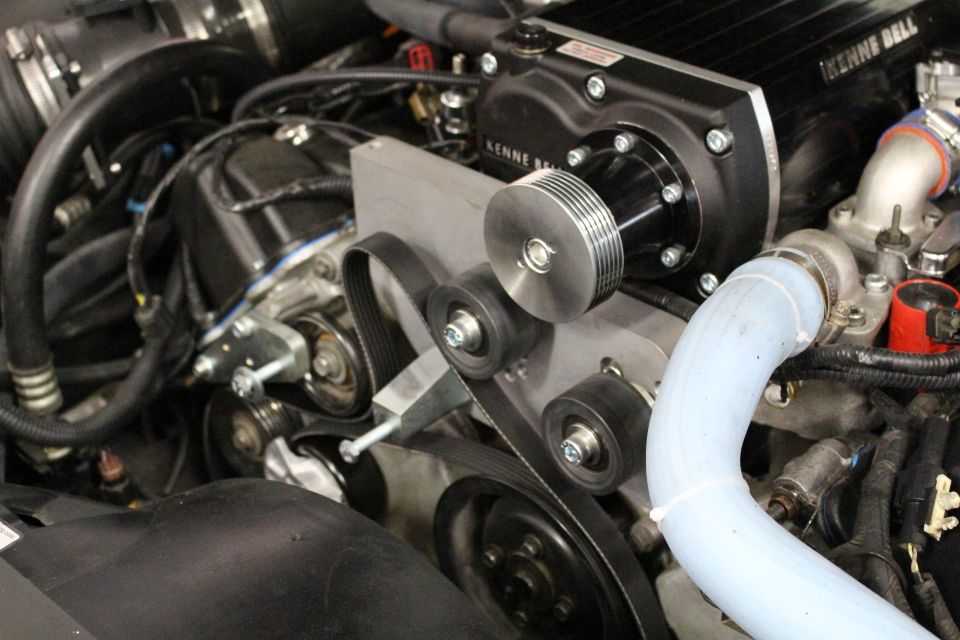 Close-up of a Kenne Bell supercharger with serpentine belt and blue coolant tube